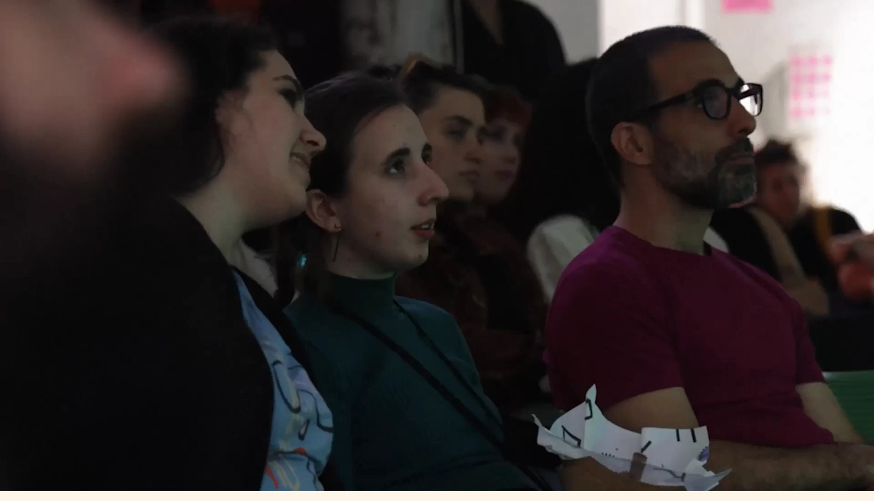 An immersive, candid video capture of audience members listening intently in a dimly lit conference setting.