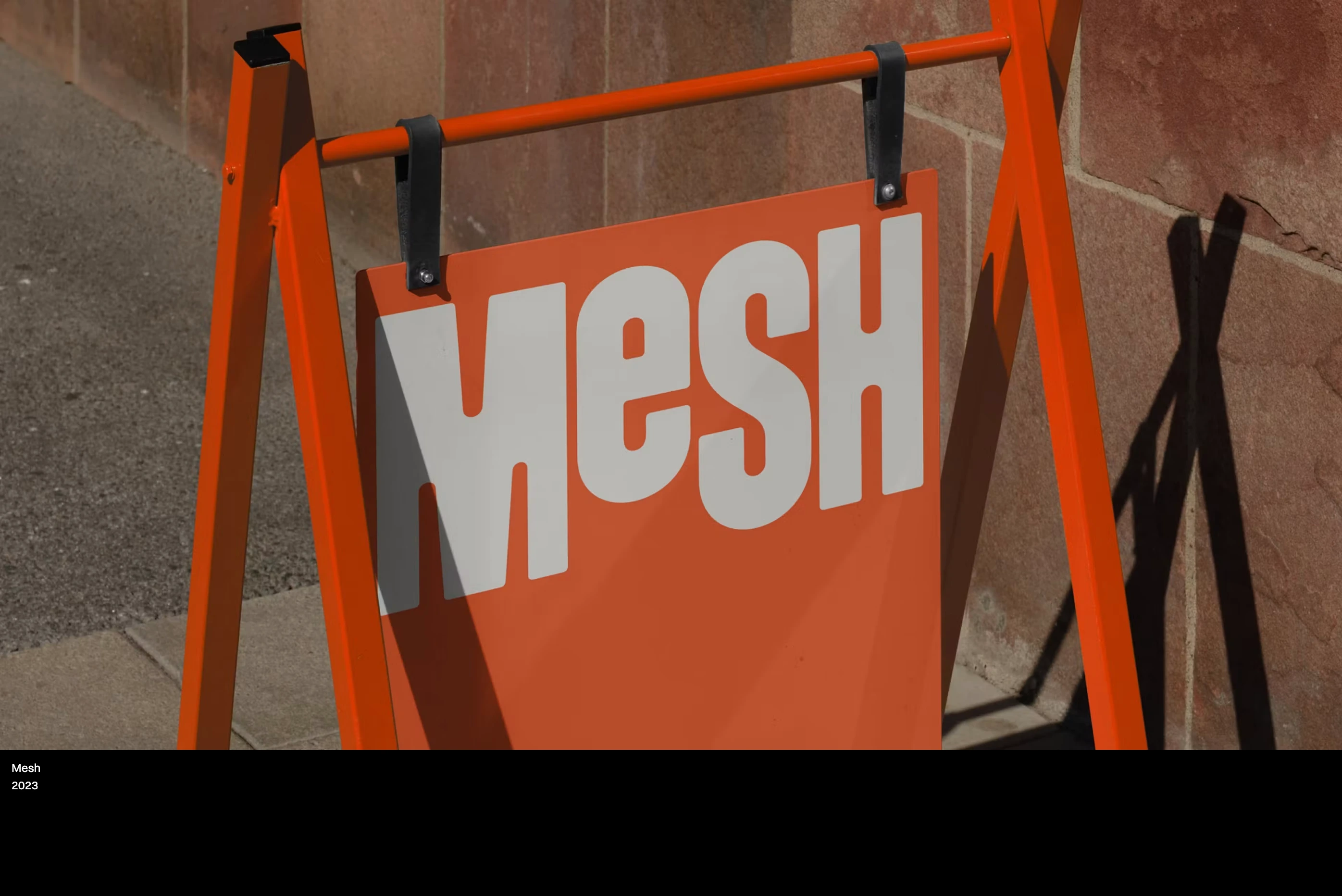 Full-bleed physical brand showcase featuring vibrant orange signage framed by restrained, corner-anchored typography.