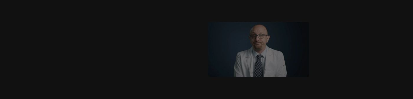 An enigmatic, intensely quiet dark space anchored by an off-center cinematic video portrait of a doctor.