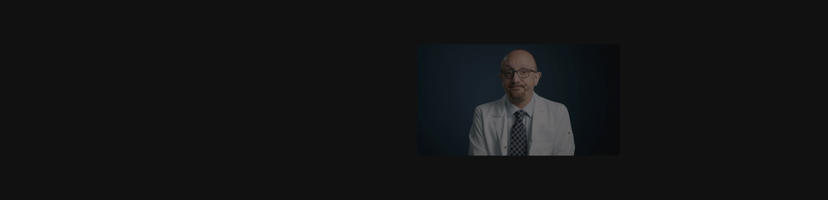 An enigmatic, intensely quiet dark space anchored by an off-center cinematic video portrait of a doctor.